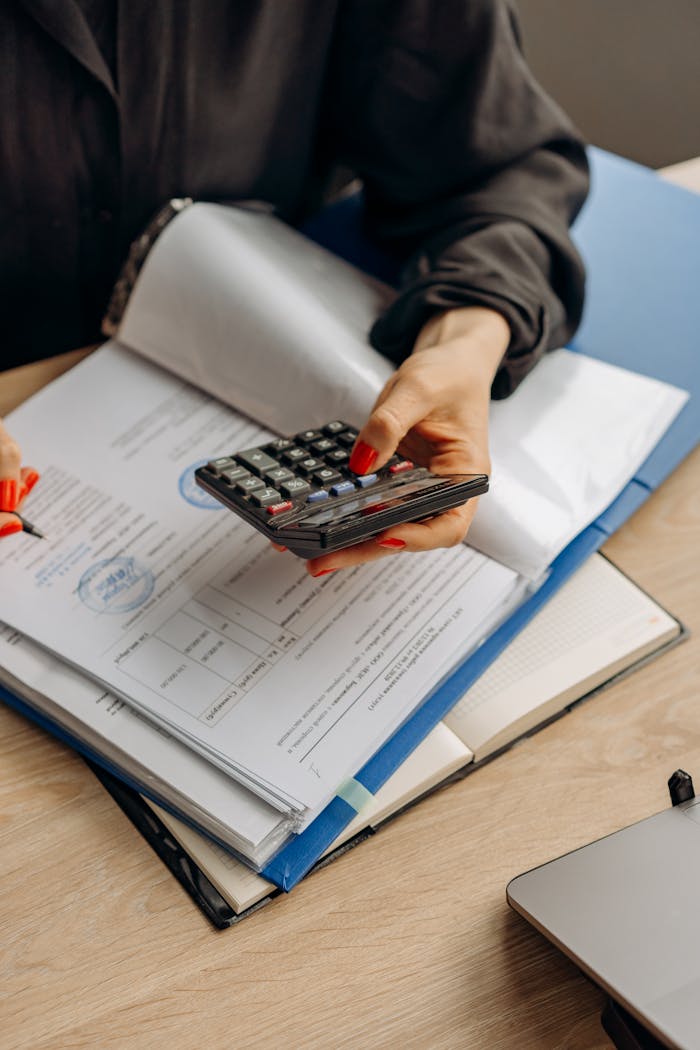 Person using calculator and documents for accounting tasks in an office setting.